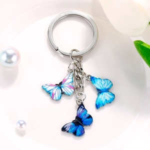 Close-up of three blue butterfly pendants on a silver keychain over white pearls