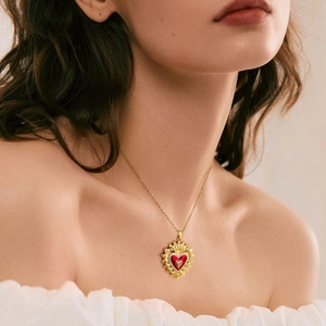 Dettaglio di una collana con ciondolo a cuore dorato con pietra rossa e zirconi su modella
