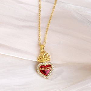 Dettaglio di una collana dorata con ciondolo a cuore in smalto rosso e zirconi su seta