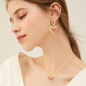 Detailed view of pink and white zircon heart pendant necklace and matching earrings on model