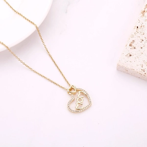 Close-up of golden heart pendant with mom script and sparkling crystals on stone