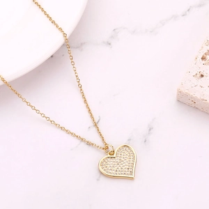 Macro shot of gold heart pendant encrusted with white cubic zirconia on a marble surface