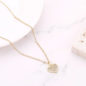 Close-up of golden heart pendant necklace with pavé micro-inlaid stones on marble