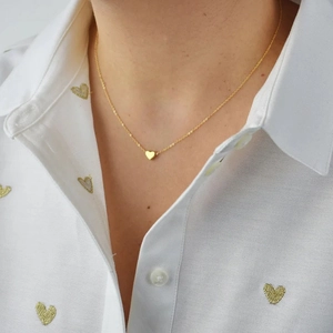 Close-up of a minimalist gold necklace with a delicate 3D heart pendant on a model