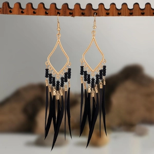 Detail of bohemian drop earrings with black beads and feather fringe on a wooden display
