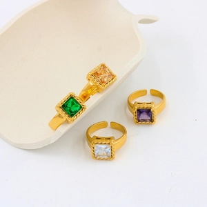 Macro detail of four gold stainless steel rings with square emerald, amber, and purple gems