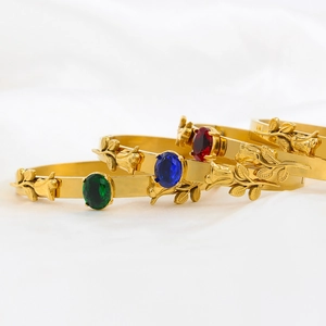 Detail of three gold bangles with rose engravings and emerald, sapphire, and ruby gemstones