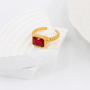 Macro detail of gold-plated twisted band ring featuring a rectangular red zircon stone