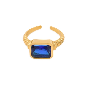 Détail de la bague ajustable dorée avec une grande pierre bleue rectangulaire et un anneau torsadé