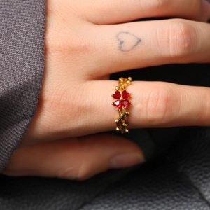 Detail of red heart-shaped gemstone clover ring with golden vine band on finger