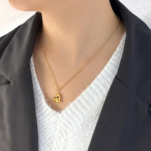 Detalle de un collar vintage dorado con colgante de corazón y circonitas rojas en modelo