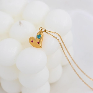 Detalle del collar de corazón dorado con circonitas azules y rosas sobre fondo de vela