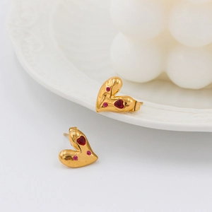 Detalle de pendientes de corazón vintage con circonitas rojas y metal dorado texturizado