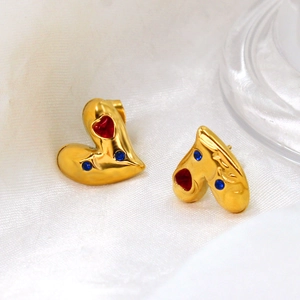 Detalle de pendientes de corazón dorados con circonitas rojas y azules sobre seda