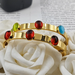Detail of 18k gold plated stainless steel bangles with colorful oval gemstones on rose petals