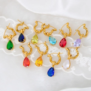 Detailed view of colorful teardrop zircon earrings with golden twisted hoops on white satin