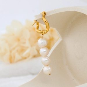 Detail of gold U-shaped earrings with four hanging freshwater pearls on a ceramic stand