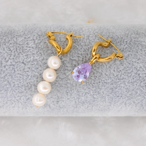 Macro shot of asymmetrical gold earrings featuring fresh water pearls and purple zircon