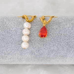 Detail of asymmetric gold earrings with freshwater pearls and red teardrop zircon stones