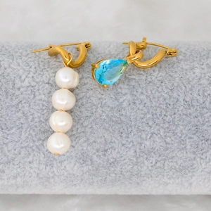 Detailed view of asymmetric earrings with white pearls and a blue pear-cut zircon stone