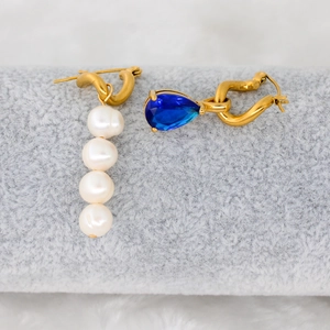 Detailed close-up of asymmetric gold earrings with white pearls and a blue teardrop zircon