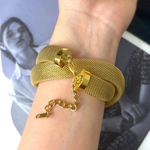 Dettaglio di un bracciale a maglia dorata con chiusura a moschettone e catena regolabile al polso