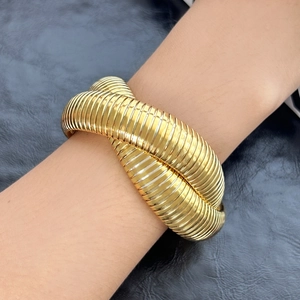 Detailansicht eines goldenen zweilagigen Spiralarmbands am Handgelenk eines Modells