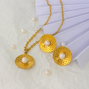 Dettaglio del set collana e orecchini in oro martellato con perle su sfondo bianco