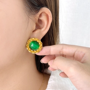 Close-up of vintage gold braided earrings with round green stones worn on ear