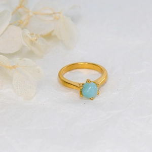 Detailed view of 18K gold plated ring with a round light blue gemstone in 4-prong setting