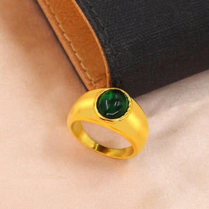 Gros plan d'une bague dorée avec pierre ovale vert émeraude sur fond de soie et de cuir