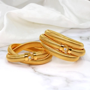 Macro detail of golden spiral tubogas bracelets with single zircon stone on marble surface