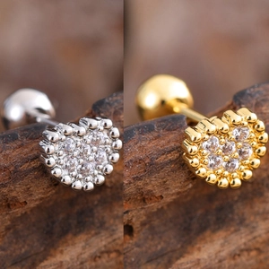 Detail of gold and silver heart cartilage studs with micro zircons on wood