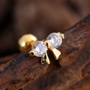 Macro shot of gold-plated bow earring with zircons and ball back on wooden texture