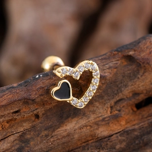 Macro shot of gold heart stud earring with black enamel and zircons on dark wood