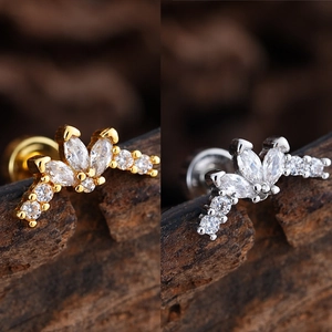 Primer plano de pendientes de corona con circonitas en oro y plata sobre madera