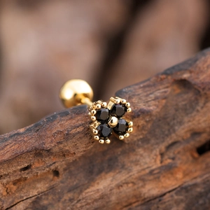 Macro shot of gold floral ear stud with black zircon petals resting on dark wood bark