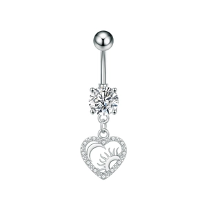 Detalle del piercing de ombligo plateado con colgante de corazón y grabados de sol y luna