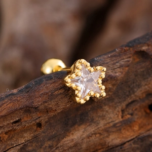 Macro view of gold star stud earring with clear zircon and beaded edge on wood background