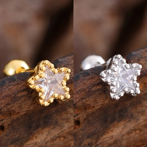 Macro shot of gold and silver star-shaped zircon ear studs with bead edge on wood background