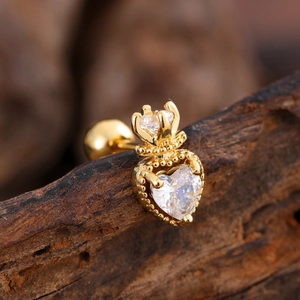 Macro detail of gold crown and heart-shaped zircon earrings on dark wood surface