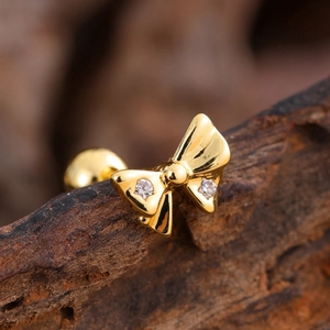 Macro shot of gold bow stud earring with zircons and ball screw back on dark bark