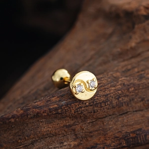 Macro detail of gold stud earring with two clear cubic zirconia on a dark wooden block