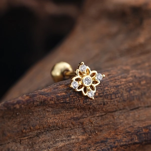 Macro shot of gold floral tragus stud with zircon stones on dark wood background