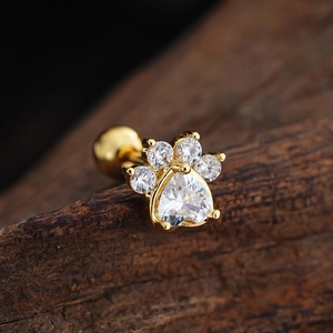 Macro shot of gold cat paw ear stud with heart-shaped cubic zirconia on dark wood