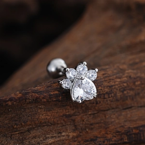 Macro detail of silver paw print stud earring with heart zircon on rustic wood