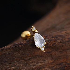 Macro shot of gold-plated pear-cut zircon cartilage stud on a rustic wooden background