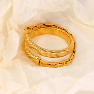 Detailed view of gold snake-pattern cuff and H-link chain bracelet on white paper