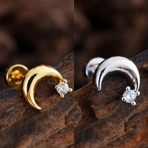 Detalle de pendientes de luna en color oro y plata con circonita sobre fondo madera