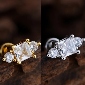 Detalle de pendientes de circonita cuadrada bañados en oro y plata sobre fondo oscuro